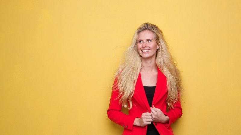 A woman in red jacket standing next to yellow wall.